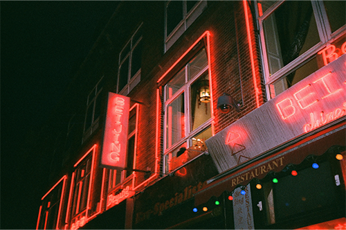 looking up at windows above a shop, each outlined in red neon. The sign of the chines restaurant reads BEIJING and there is another vertical BEIJING neon sign between the windows